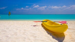 Una playa con un kayak amarillo y una pala rosa en la arena.