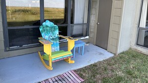 Une chaise à bascule colorée et une petite table sont placées devant un bâtiment doté de grandes fenêtres.