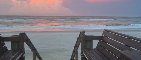 Een houten looppad naar een strand, met een zonsondergang op de achtergrond.