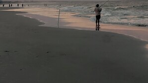 Escena de playa con una persona pescando, mar tranquilo y cielo al atardecer.