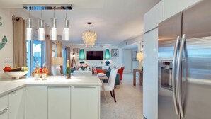 Eine moderne Küche mit einem Edelstahl-Kühlschrank, eine Essecke mit Tisch und Stühlen sowie ein Wohnzimmer mit Sofa und Fernseher.