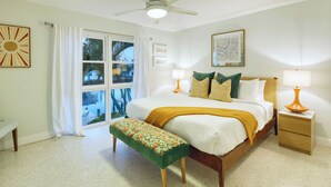 Ein Schlafzimmer mit einem Bett, zwei Nachttischlampen, einer Bank, einem Deckenventilator und einem Fenster mit Vorhängen.