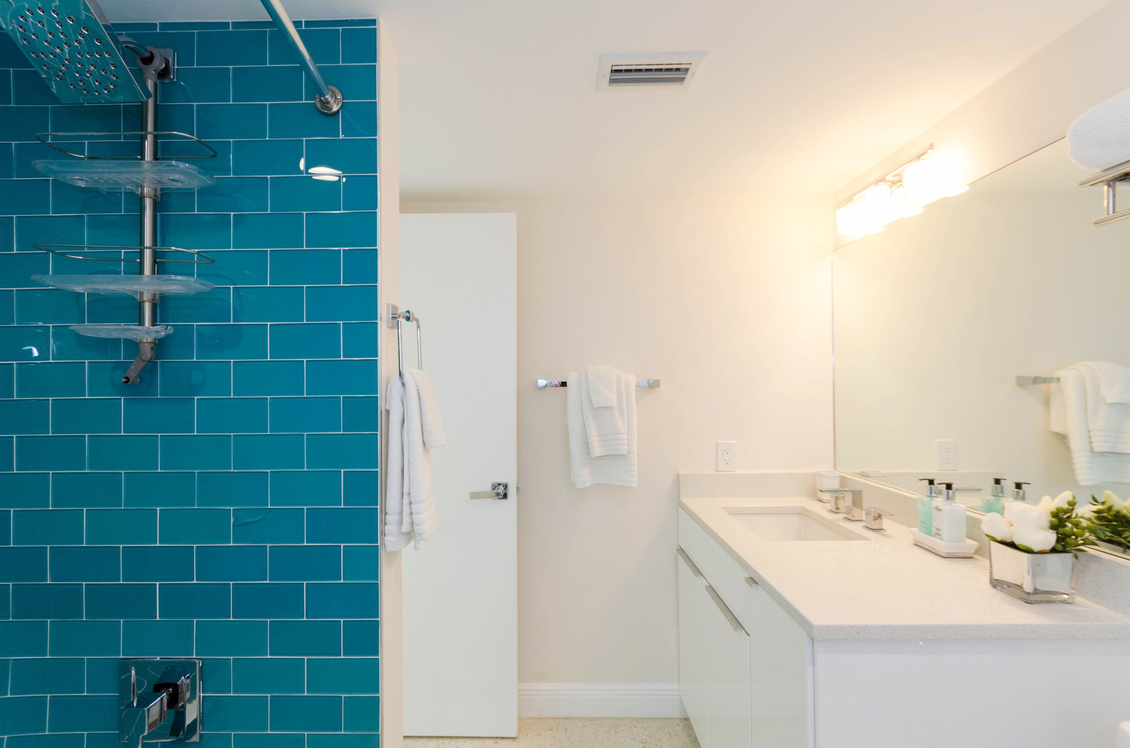 A bathroom with a blue tiled wall, a white sink, a mirror, and a shower with a glass enclosure.