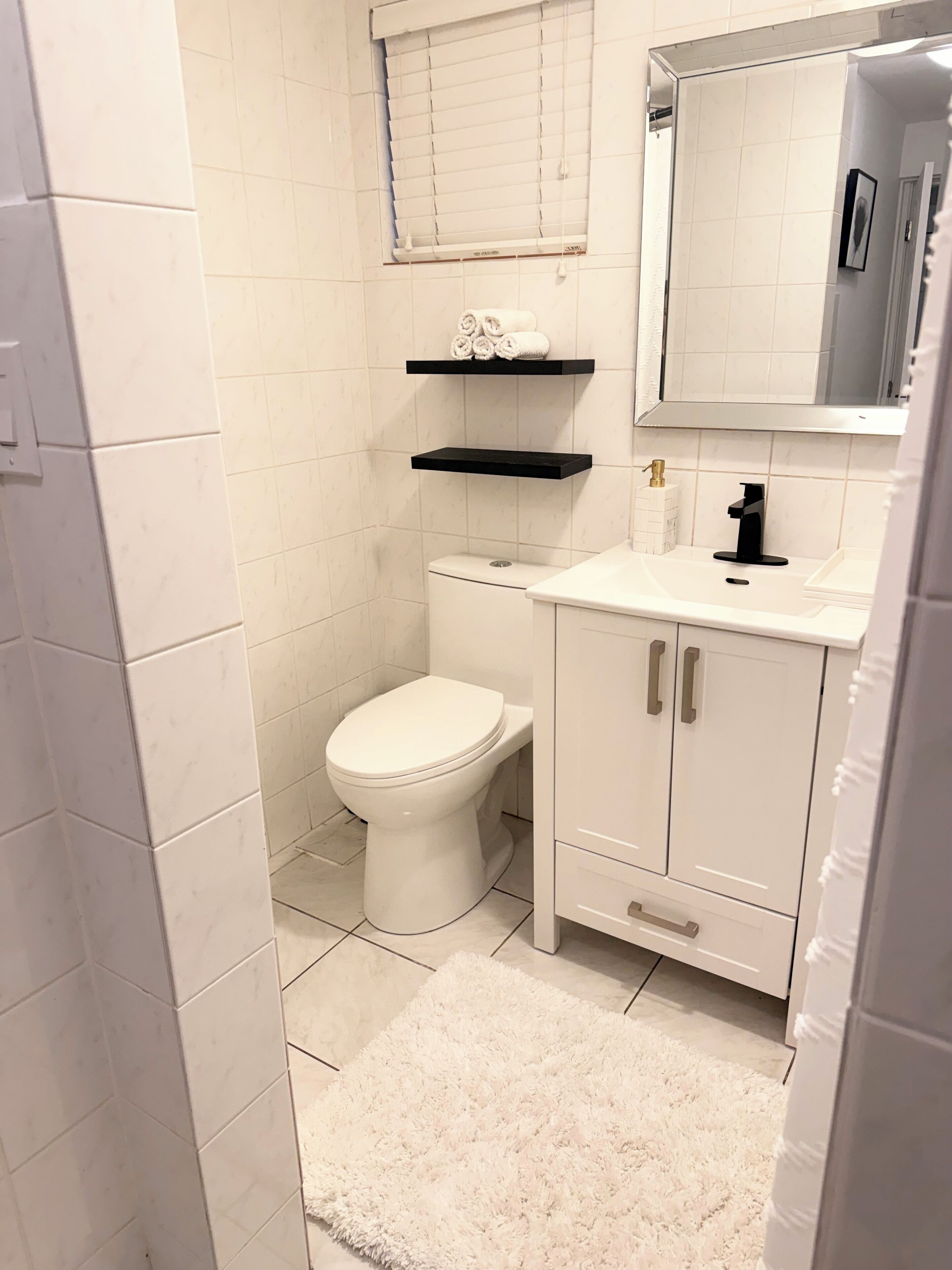 A bathroom with a toilet, a sink, a mirror, and two shelves with towels.