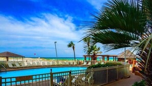 A pool area with a view of the beach, lounge chairs, and a fenced deck.