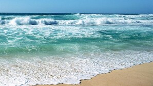 A beach with waves crashing onto the shore under a clear blue sky.