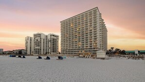 A high-rise hotel with multiple floors and balconies, situated on a beach with tents and beach equipment.