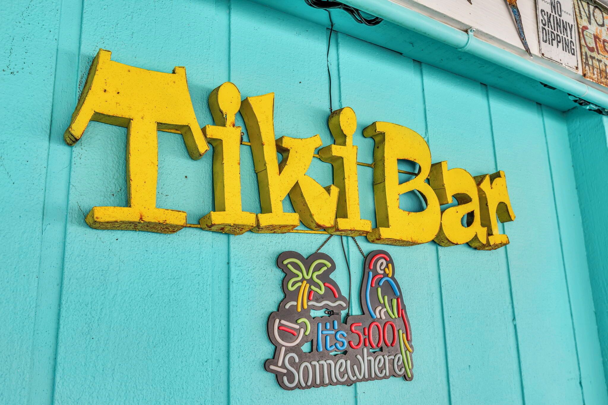 Een bord met de tekst 'Tiki Bar', voorzien van een kleurrijk ontwerp en de zin 'It's 500 Somewhere' eronder.
