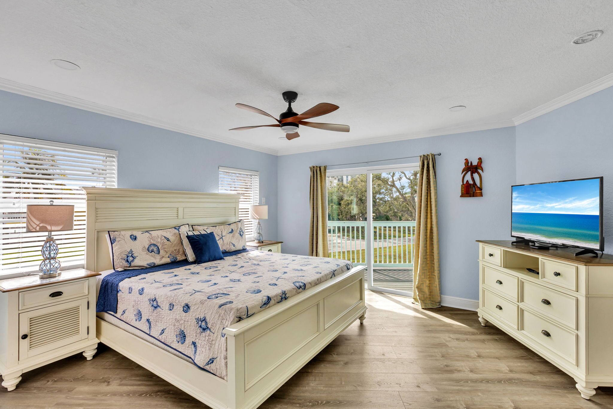A bedroom with a bed, a TV, a ceiling fan, and a balcony with curtains.