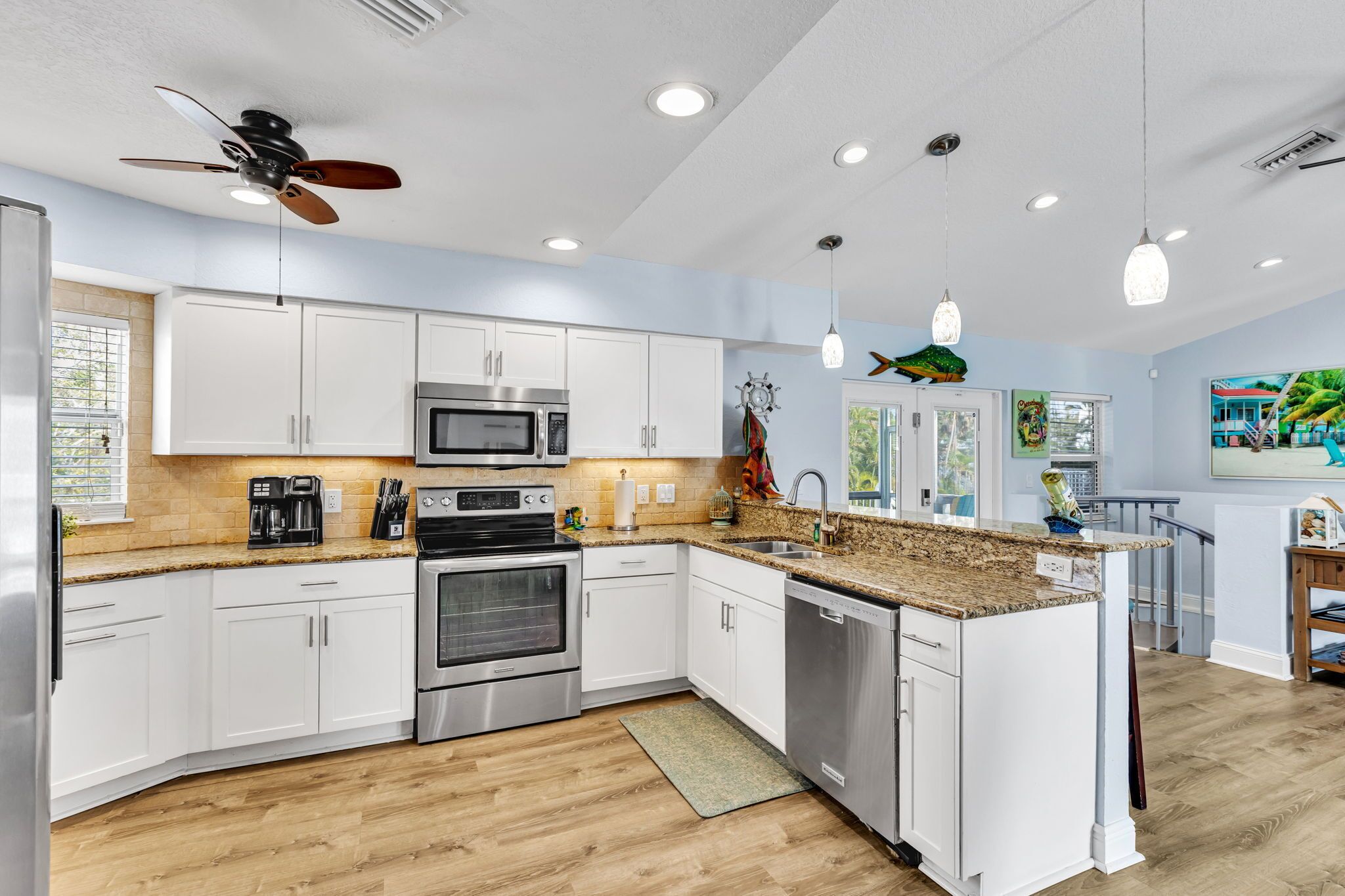 A modern kitchen with white cabinets, stainless steel appliances, a granite countertop, and a ceiling fan.