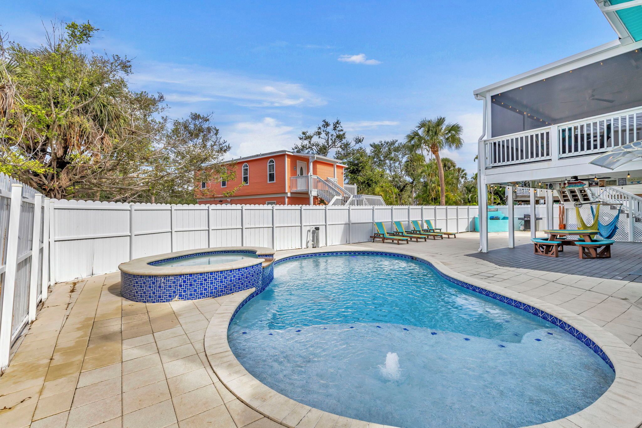 A swimming pool with a blue mosaic border, a white fence, and a red building in the background.