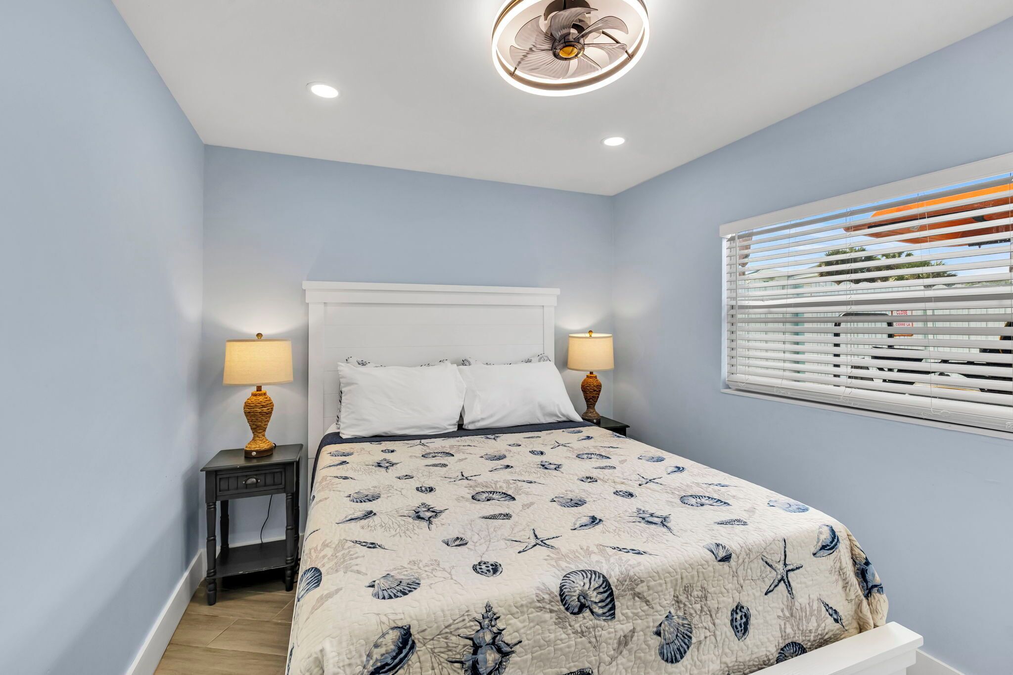 A bedroom with a bed, two bedside tables, a ceiling fan, and a window with blinds.