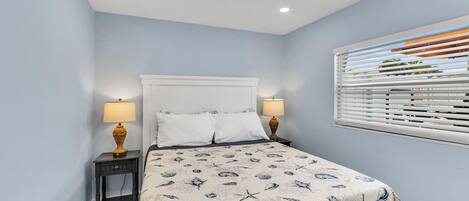 A bedroom with a bed, two bedside tables, a ceiling fan, and a window with blinds.