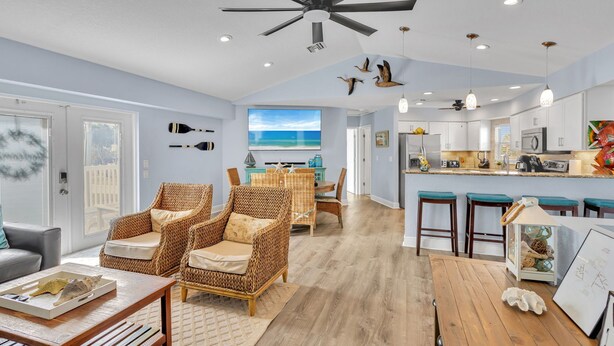 A spacious living room with wicker furniture, a wooden dining table, and a view of the ocean through large windows.
