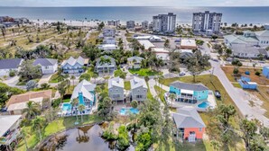 An aerial view of a coastal residential area with houses, a swimming pool, and a view of the ocean.
