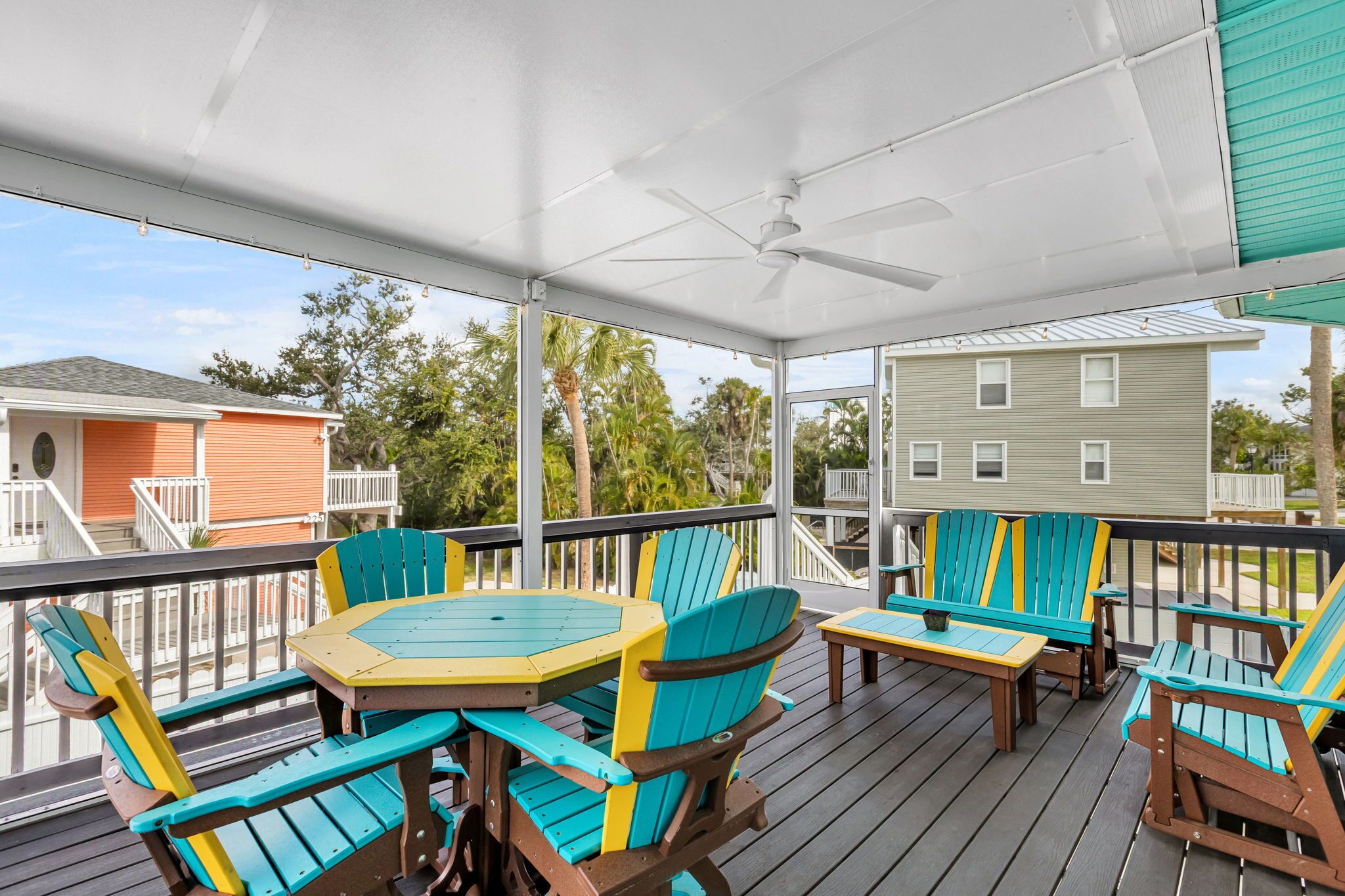 A covered outdoor deck with a table and chairs, a ceiling fan, and a view of neighboring houses.