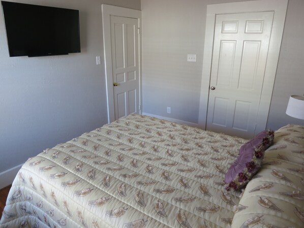 Un dormitorio con una cama, dos puertas, un televisor de pantalla plana y una lámpara.