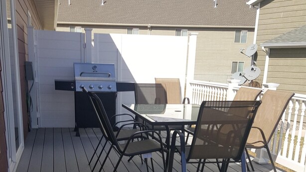 Een terras buiten met een barbecue, stoelen en een tafel.