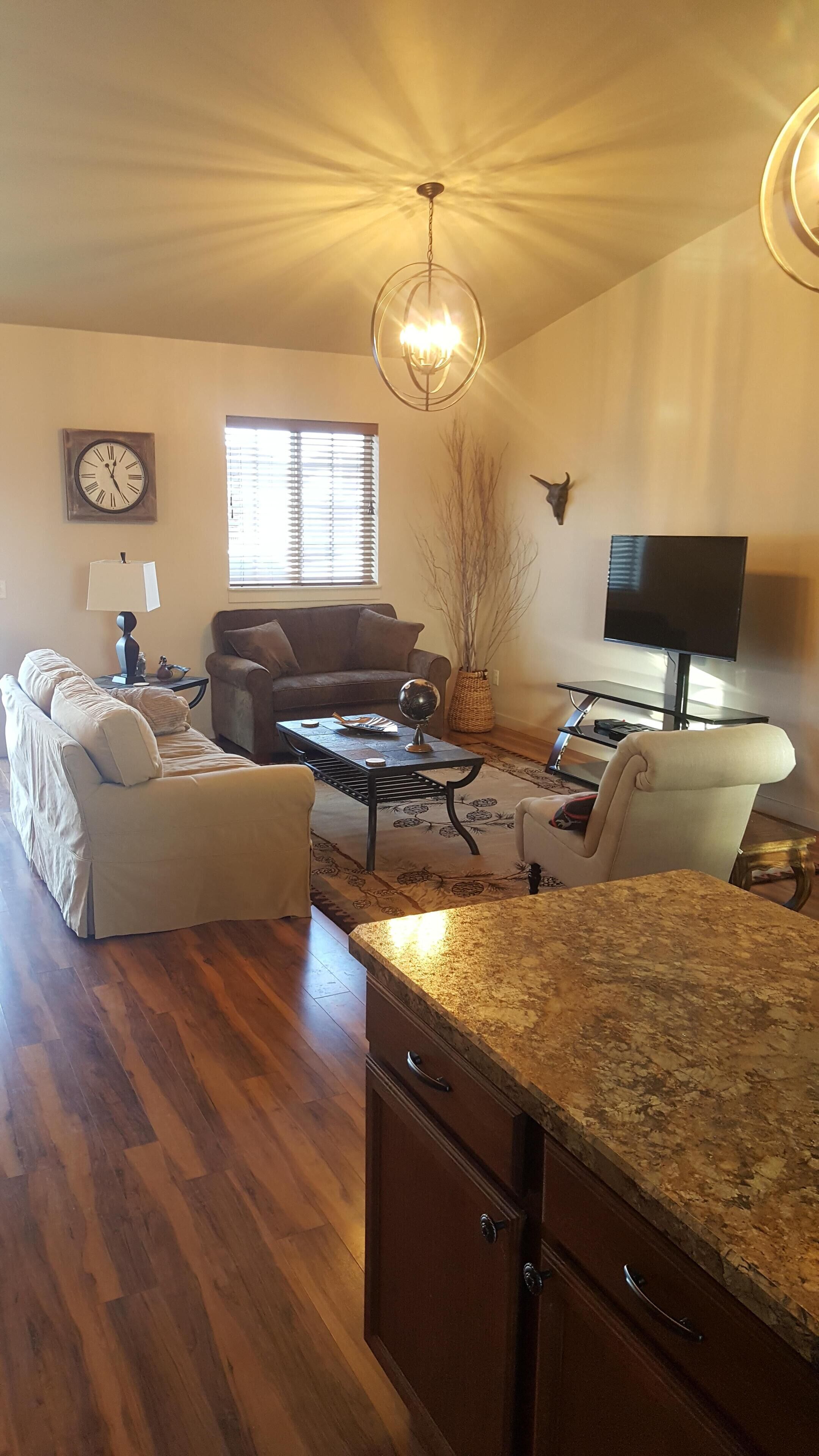 A spacious living room with a wooden floor, a sofa, a coffee table, a TV, and a chandelier.