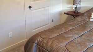 Een slaapkamer met een bed, een deur, een klein tafeltje met een lamp en een wandplank.