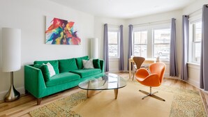 Una sala moderna con un sofá verde, una mesa de centro de vidrio y sillones naranjas.