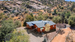 A cabin with a metal roof, surrounded by dry vegetation and rocky terrain, with a mountain in the background. - Quaint Cabin With Spectacular Views Of The Granite Dells, Great Hiking/Kayaking! (Prescott)