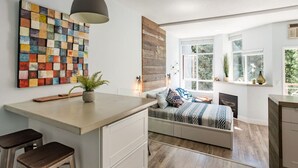 A modern bedroom with a bed, bedside table, and a large window. - Village Modernist Studio - Hottub & Pool (Whistler)
