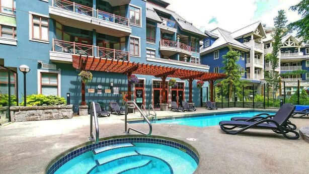A hotel with a swimming pool, lounge chairs, and a covered patio area. - Village Modernist Studio - Hottub & Pool (Whistler)