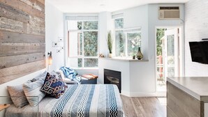 A modern bedroom with a large bed, a wooden accent wall, and a view of the outdoors. - Village Modernist Studio - Hottub & Pool (Whistler)