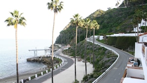 Eine Küstenstraße mit Palmen, einem Strand und einem weißen Gebäude mit Balkon.