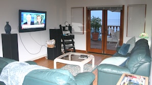 Ein Wohnzimmer mit Fernseher, Sofa, Couchtisch und Blick ins Freie.