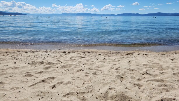 A beach with clear blue water, a sandy shore, and distant mountains. -  Lake and Mountain Escape (Incline Village)