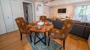 A dining area with a round table set for four, surrounded by patterned chairs. A sofa and a flat-screen TV are visible in the background. -  Lake and Mountain Escape (Incline Village)