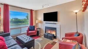 Une chambre d’hôtel moderne dotée d’une grande fenêtre, d’une cheminée, d’un téléviseur à écran plat et de meubles en cuir rouge.