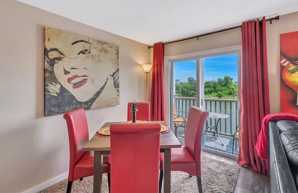 A dining area with a table and chairs, a large painting on the wall, and a view of the outdoors through a sliding glass door. - ❤️of DWTN on the RIVER/Walk 2 BROADWAY & ALL/❤️2KING BDS/2BA/Free PRKG/POOL!🎸🎻 (Nashville)