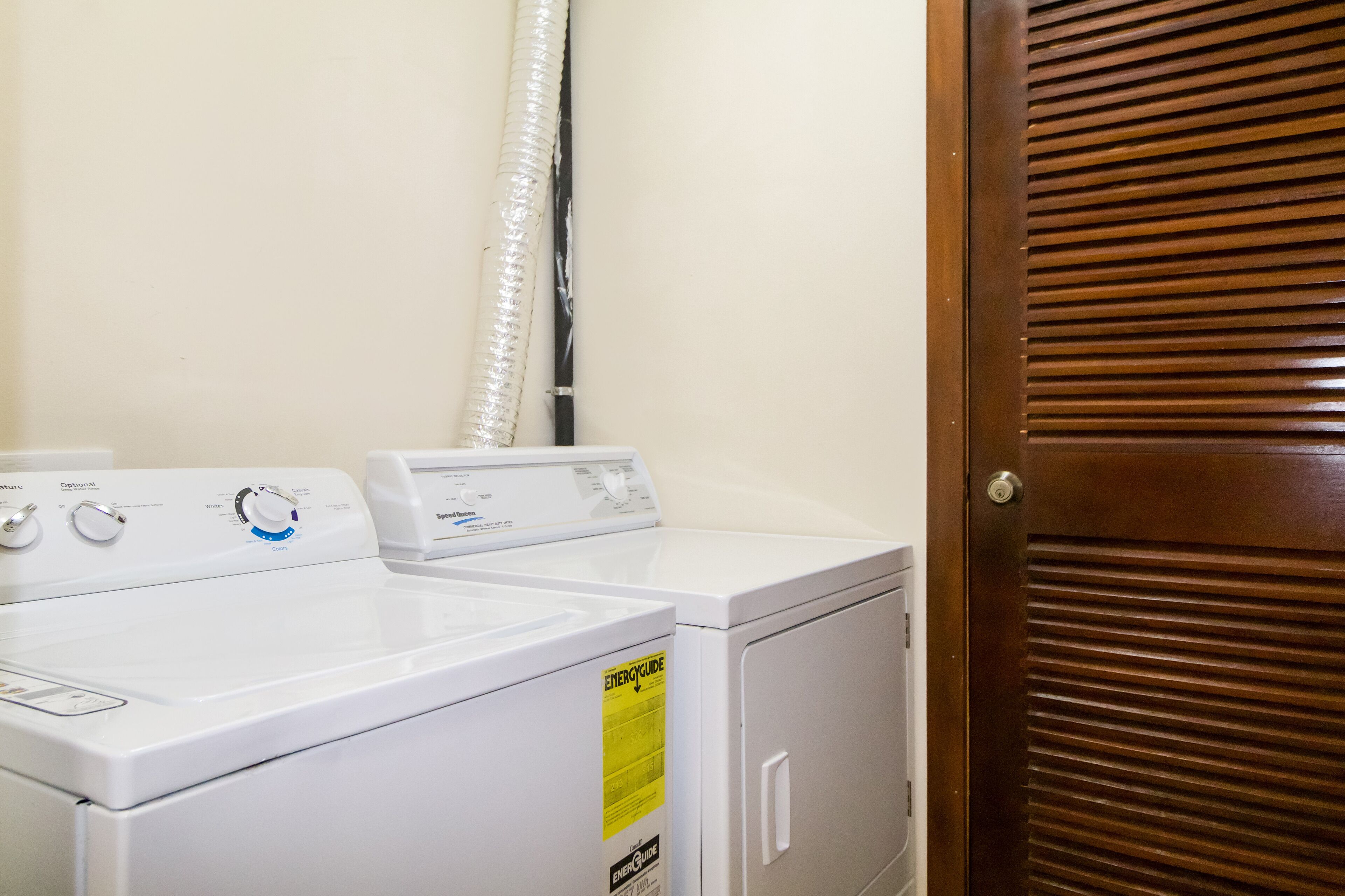 A laundry area with two white washing machines and a dryer, a wooden door, and a visible vent pipe.