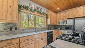 A kitchen with wooden cabinets, a stainless steel refrigerator, a gas stove, and a window with a view of trees. - Luxury Ski or Hiking retreat- 2 KING beds and more! (Park City)