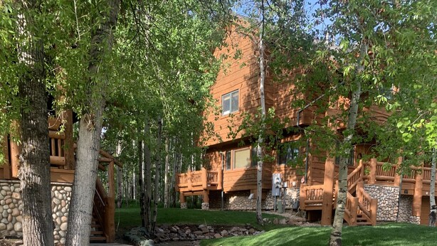 A wooden cabin with a stone foundation, surrounded by a well-maintained lawn and a small stream. - Luxury Ski or Hiking retreat- 2 KING beds and more! (Park City)