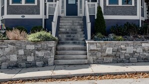Una casa de dos pisos con un porche delantero, escalones de piedra y un camino de entrada.