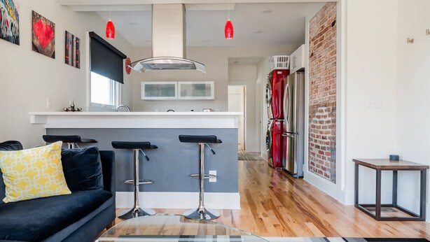 Una cocina moderna con una isla central, taburetes de bar y un refrigerador rojo.
