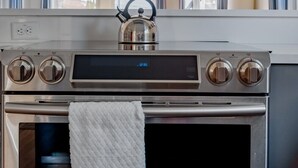 Una cocina moderna con extractor de acero inoxidable, un hervidor en la estufa y un reloj digital que marca las 12:35.