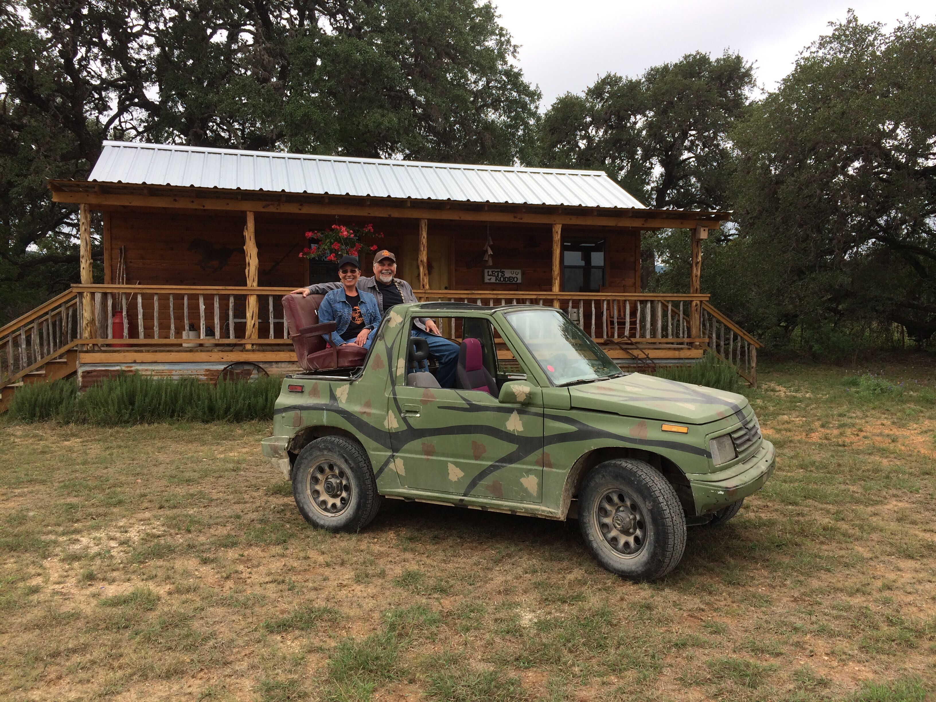 A green military-style vehicle parked in front of a wooden cabin with a porch and a sign that reads "Let's Rodeo".
