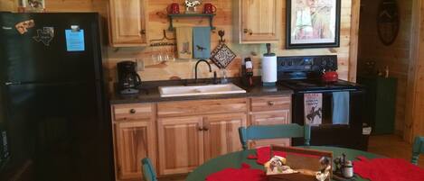 A wooden cabin interior with a kitchen area, including a refrigerator, stove, sink, and wooden cabinets.