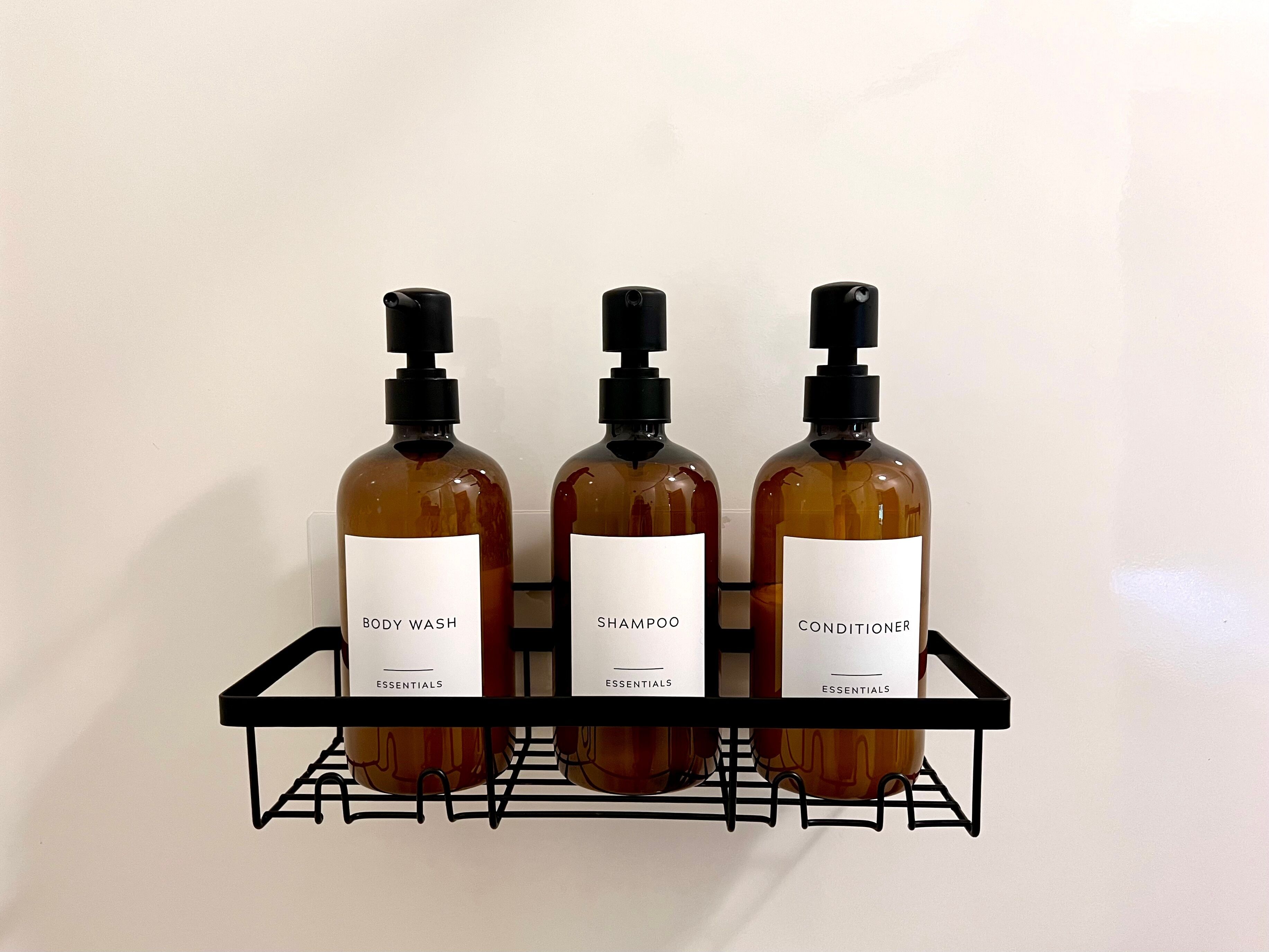 Three bottles of body wash, shampoo, and conditioner on a black metal shelf against a white wall.