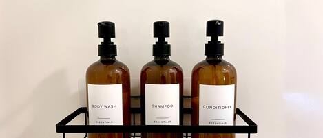 Three bottles of body wash, shampoo, and conditioner on a black metal shelf against a white wall.