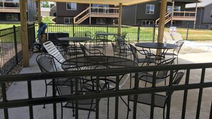An outdoor patio area with metal tables and chairs, a covered seating area, and a view of residential buildings in the background.