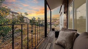 Un balcón con vista a un atardecer, una terraza de madera y un sofá con cojines.