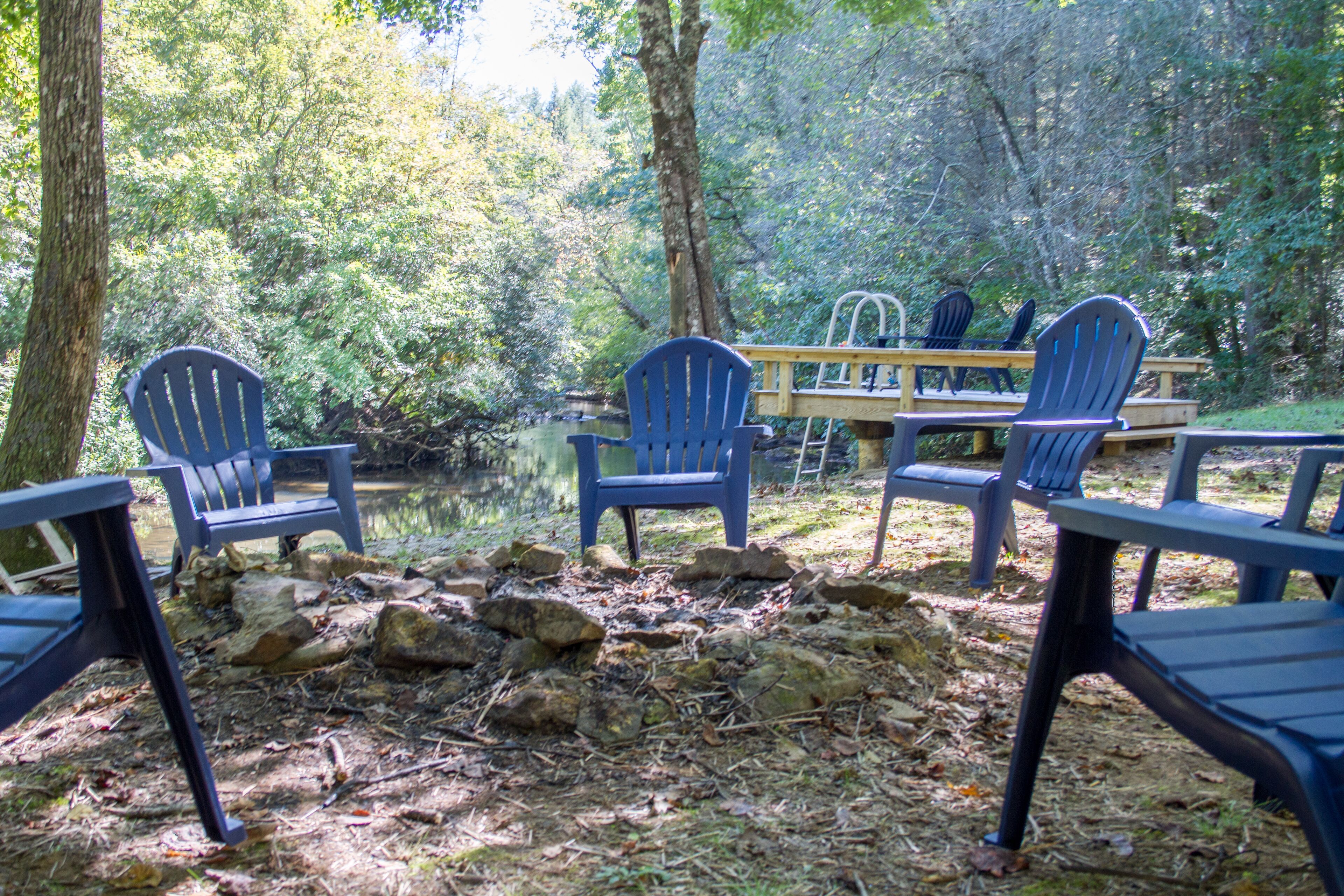 A campsite with several Adirondack chairs and picnic tables around a small pond, surrounded by trees.