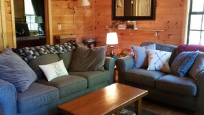 A cozy log cabin interior with two sofas, a coffee table, and a bookshelf. - Wonderful cabin on Fightingtown Creek, sleeps 8 (Epworth)