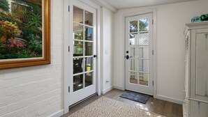 A hallway with white brick walls, a framed painting, a white door with glass panels, and a white cabinet. - Private Cottage! Easy Walk Through The Park To Encinitas And Moonlight Beach. (Encinitas)